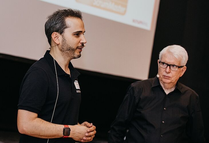 Jeff Sutherland und Peter Fischbach in einem gemeinsamen Registered Scrum Master Training Jeff Sutherland und Peter Fischbach referieren vor einer Leinwand in einem Scrum Training